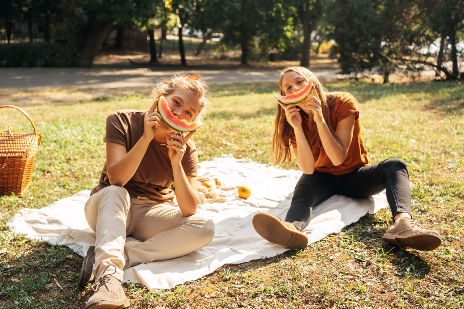 How to Organize the Perfect Picnic with Friends Group of friends sitting on a picnic blanket with baskets and watermelon outdoors
